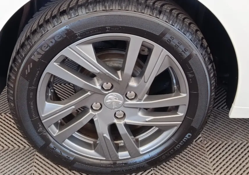 Gros plan sur la roue avant droite d'une Peugeot 208 blanche, avec jante alliage et logo lion au centre.