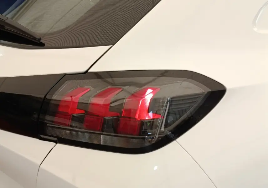 Gros plan sur le feu arrière droit rouge et noir d’une Peugeot 208 blanche vue de l’arrière.