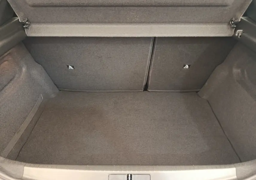 Coffre ouvert vu de face d'une Peugeot 208 blanche, espace de chargement vide et revêtement gris foncé.
