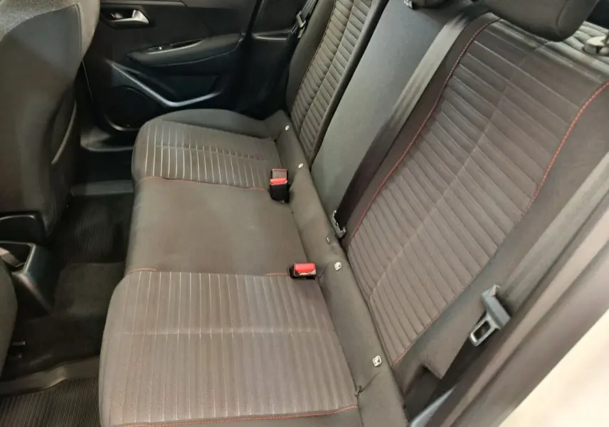 Vue intérieure côté droit montrant la banquette arrière noire avec surpiqûres rouges de la Peugeot 208 blanche.