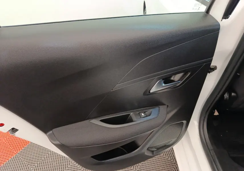 Vue rapprochée de la porte avant droite noire de la Peugeot 208 blanche, montrant la poignée et le bouton de lève-vitre.