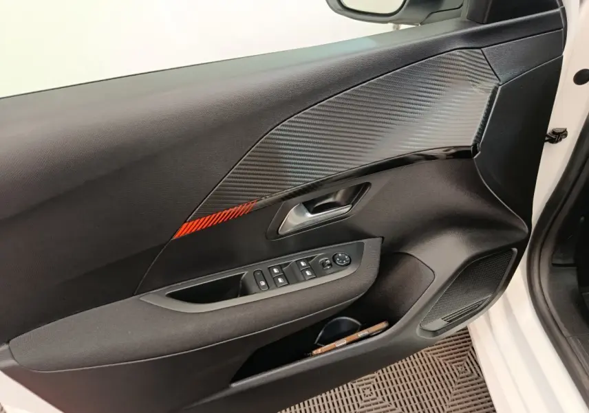 Vue intérieure côté gauche de la porte avant blanche d’une Peugeot 208 avec insert décor carbone et bande rouge.