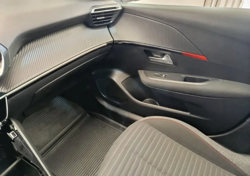 Intérieur côté passager de la Peugeot 208 PureTech 75 blanc, avec tableau de bord noir texturé et siège tissu gris à surpiqûres rouges.