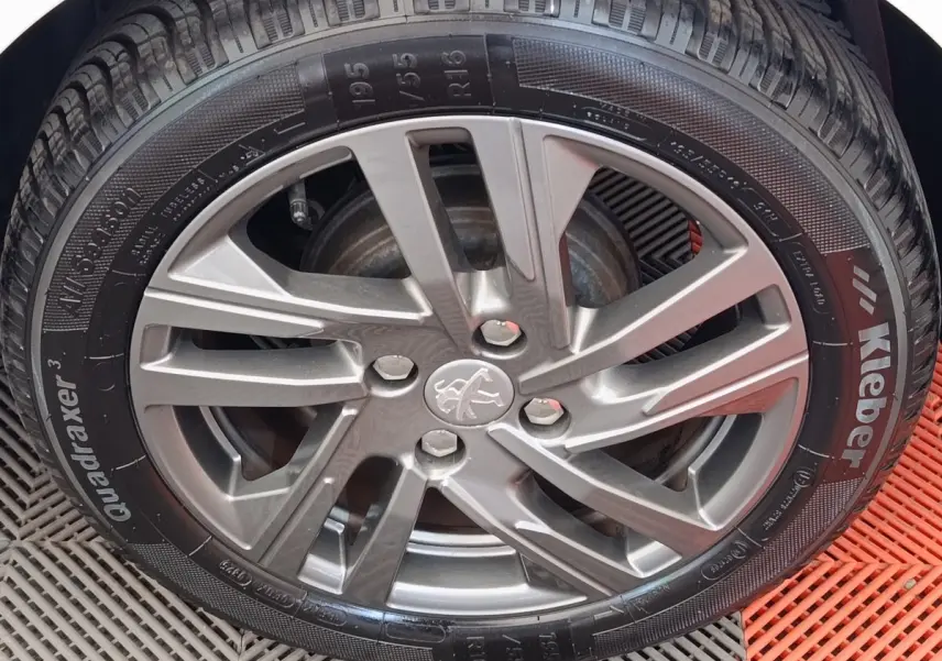 Gros plan sur la jante alliage grise et pneu Kleber d'une Peugeot 208 blanche, vue côté roue avant.