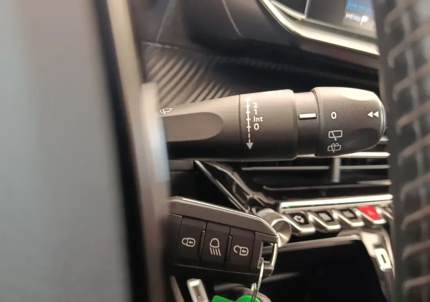Gros plan sur la manette d’essuie-glace et la clé de contact dans l’habitacle d’une Peugeot 208 blanche.