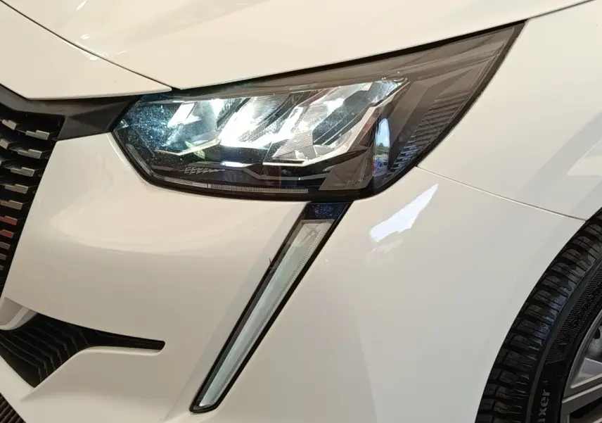 Gros plan sur le phare avant droit blanc d’une Peugeot 208 PureTech 75 S&S Active Business 2021 avec feux LED et calandre noire.