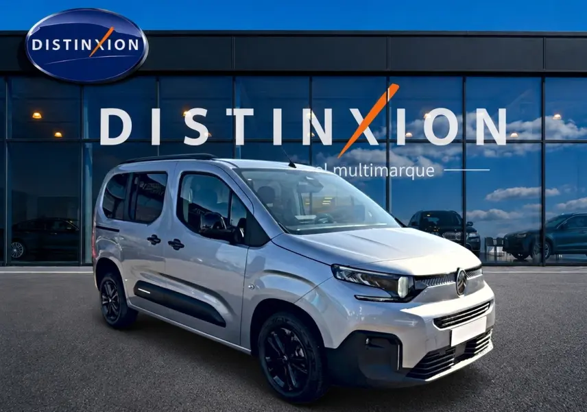 Vue 3/4 avant du Citroën Berlingo Steel Grey 2026 avec barres de toit et jantes noires devant un showroom.