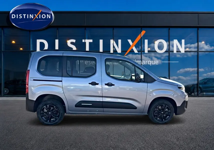 Profil droit du Citroën Berlingo 2026 steel grey avec barres de toit et jantes noires devant une vitrine Distinxion.