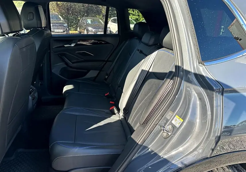 Vue intérieure côté arrière droit du Volkswagen Tiguan gris dauphin 2024, sièges en cuir noir avec surpiqûres bleues.