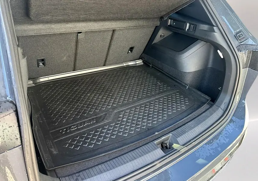 Coffre ouvert du Volkswagen Tiguan gris dauphin 2024, avec tapis de protection noir marqué Tiguan visible.