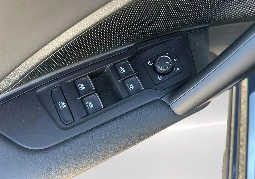Gros plan sur les commandes de lève-vitres et réglage des rétroviseurs côté conducteur du Volkswagen Tiguan gris dauphin.