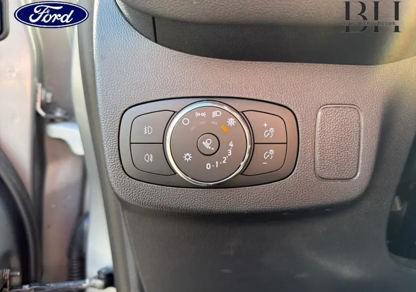Gros plan sur le bouton de réglage des phares à gauche du tableau de bord du Ford Puma gris Solar Métallisée 2024.