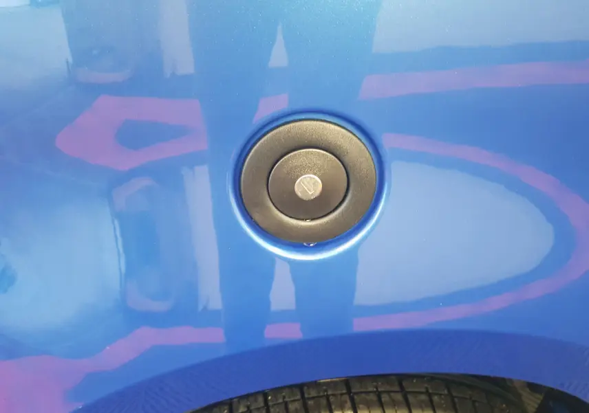 Gros plan sur la trappe de réservoir bleu d'une Aixam Ambition 0.5 City Sport, avec pneu partiellement visible en bas.