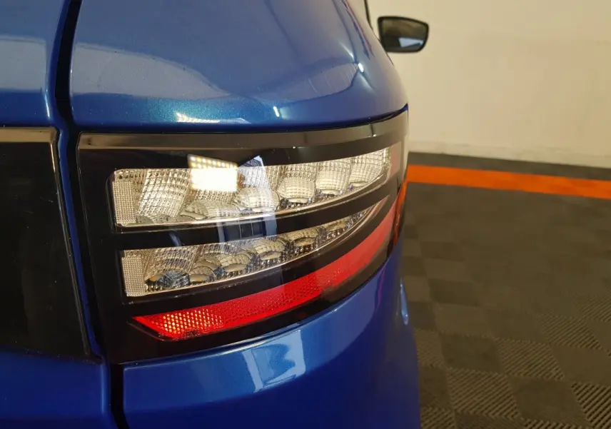 Gros plan sur le feu arrière droit bleu de l'AIXAM AMBITION 0.5 CITY SPORT avec rétroviseur caméra côté conducteur visible.