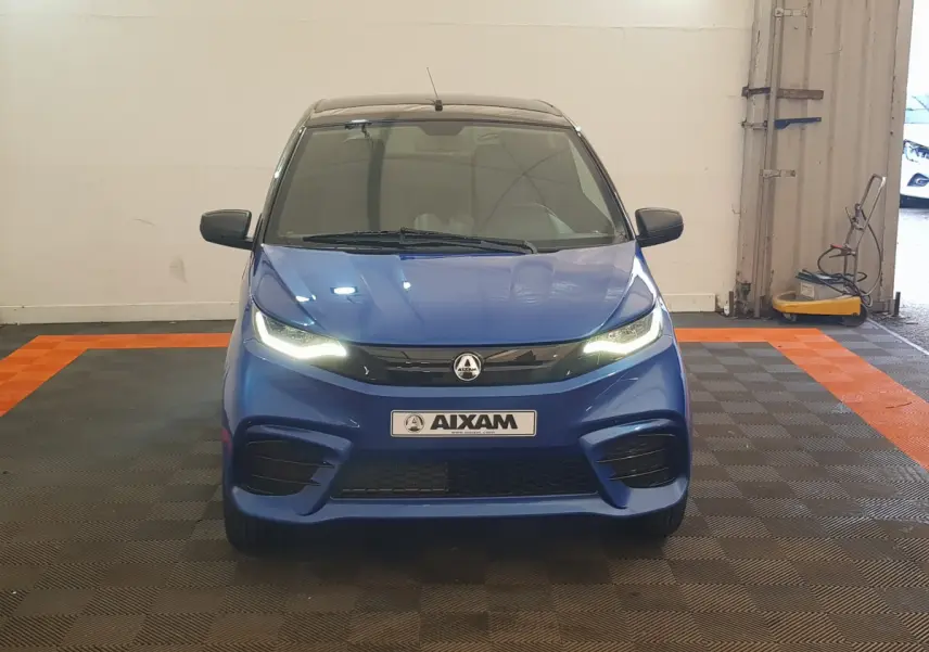 Vue frontale d'une AIXAM AMBITION 0.5 CITY SPORT bleu avec phares allumés et rétroviseur caméra côté conducteur.