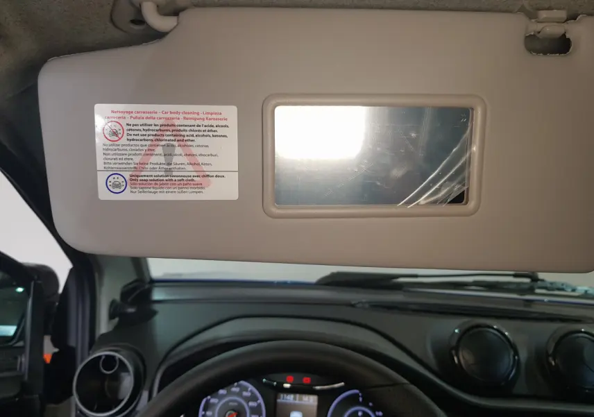 Vue intérieure centrée sur le pare-soleil côté conducteur avec miroir, tableau de bord noir et volant d'AIXAM Ambition bleu 2026.