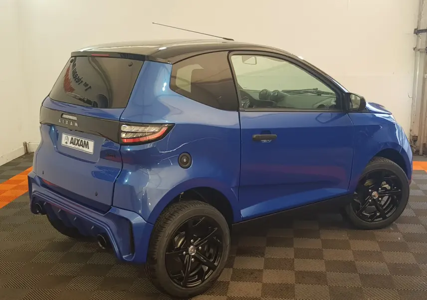 Vue 3/4 arrière droite d'une Aixam Ambition 0.5 City Sport bleu avec jantes noires et rétroviseur caméra côté gauche.
