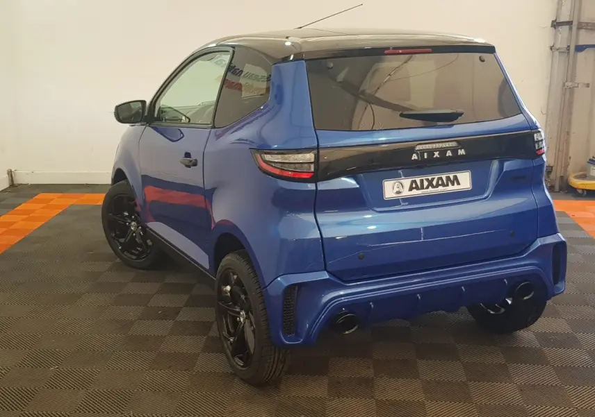 Vue 3/4 arrière d'une Aixam Ambition 0.5 City Sport bleu avec jantes noires et rétroviseur caméra côté gauche.