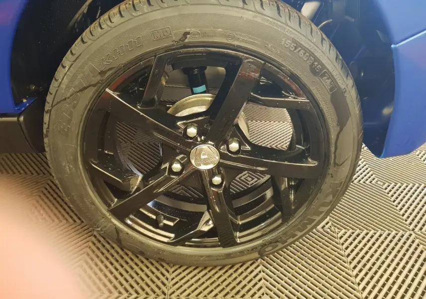 Gros plan sur la roue avant droite noire de l'AIXAM AMBITION 0.5 CITY SPORT bleu, mettant en valeur la jante sportive brillante.