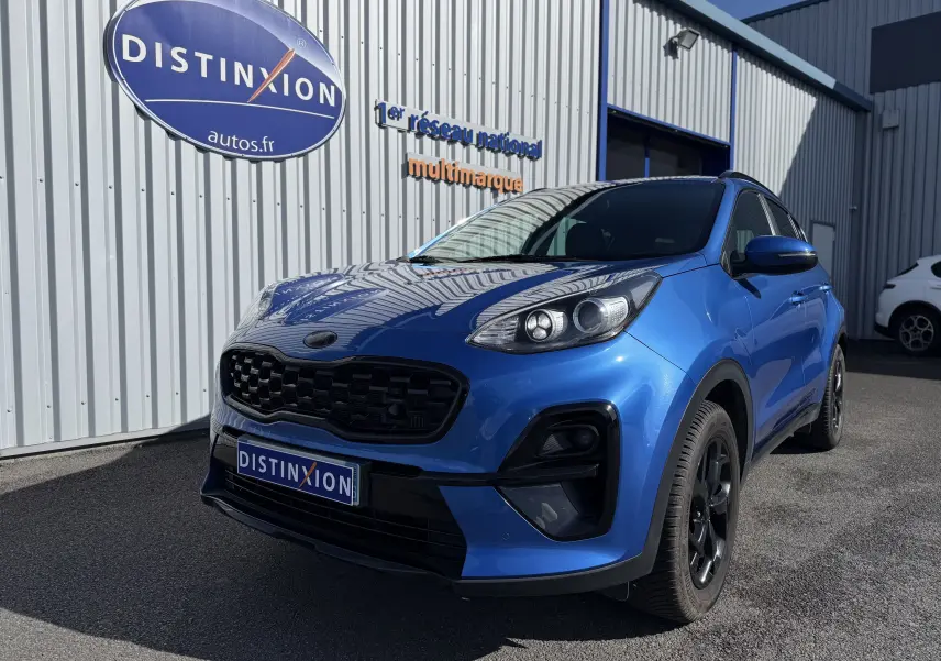 KIA Sportage 1.6 CRDI bleu en 3/4 avant droit, avec calandre noire et jantes noires, stationné devant un bâtiment.
