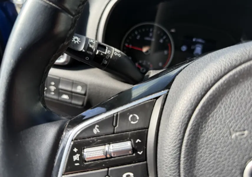 Gros plan sur les commandes au volant noir du Kia Sportage 1.6 CRDI 136 Black Edition 2021, tableau de bord flou en arrière-plan.