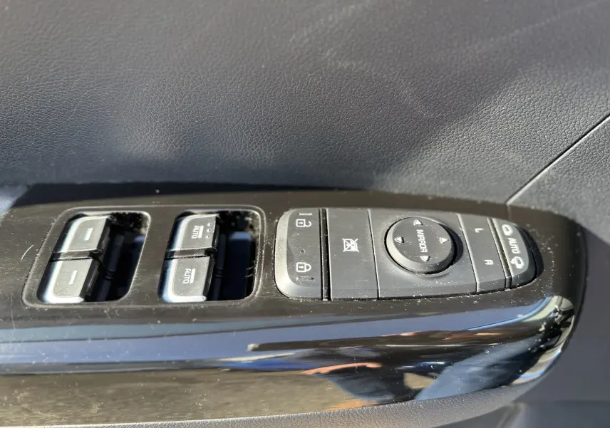 Gros plan sur les commandes de lève-vitres et rétroviseurs côté conducteur du KIA Sportage bleu 2021, finition Black Edition.