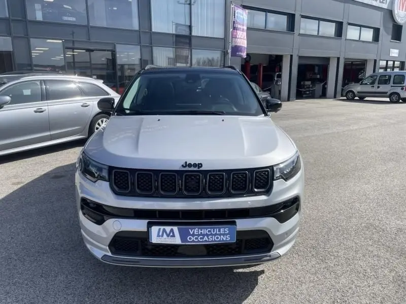 Vue frontale d'un Jeep Compass gris métal 2023 avec calandre noire et toit contrasté noir, stationné devant un garage.