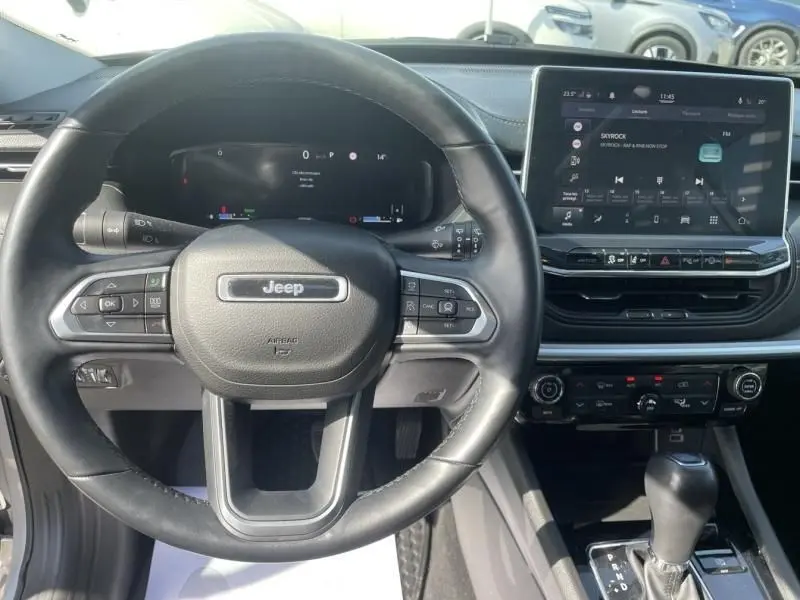 Vue intérieure centrée sur le volant noir et le tableau de bord numérique du Jeep Compass gris métal 2023 hybride essence.