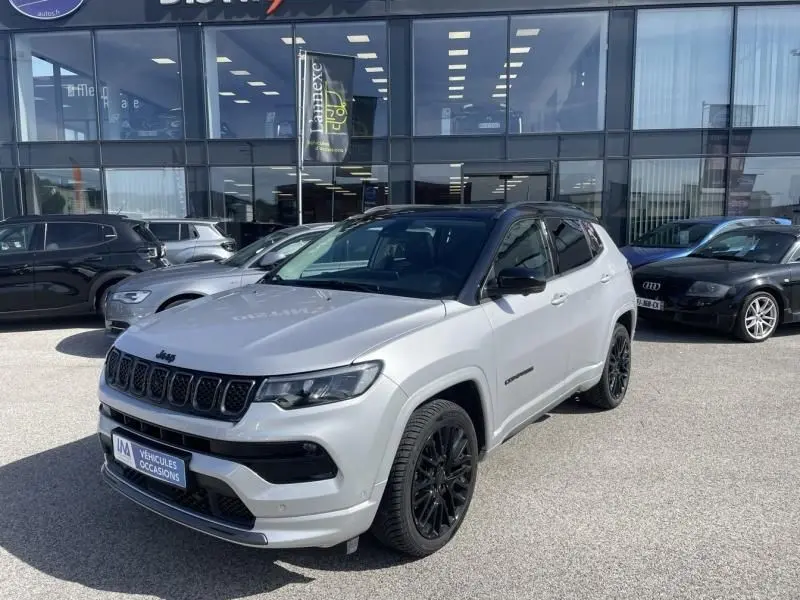 Jeep Compass gris métal en 3/4 avant droit, toit noir et jantes noires, stationné devant un showroom.
