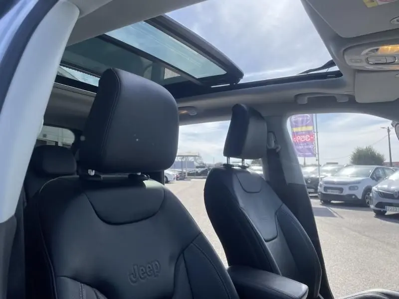 Vue intérieure du Jeep Compass 2023 montrant les sièges avant en cuir noir et le toit panoramique ouvert.