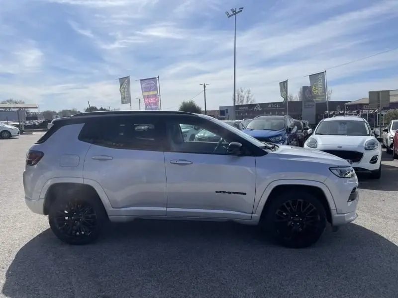 Jeep Compass gris métal vu de profil côté gauche, avec jantes noires et toit noir contrastant, stationné en extérieur.