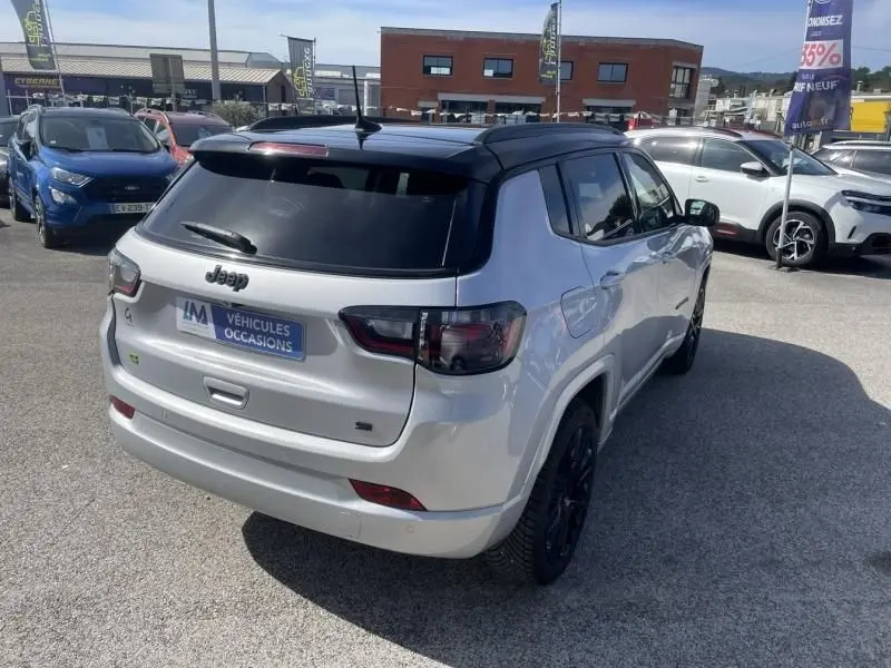 Vue 3/4 arrière droite d'un Jeep Compass gris métal 2023 avec toit noir et vitres teintées, stationné en extérieur.