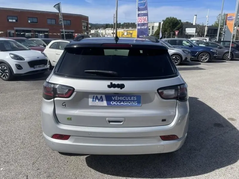 Vue arrière d’un Jeep Compass gris métal 2023 avec vitres teintées et logo hybride visible sur un parking.