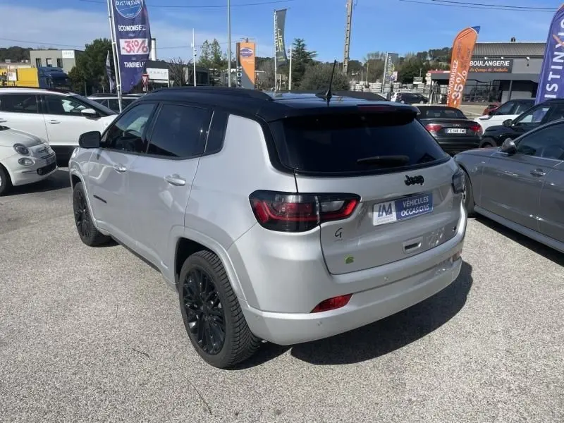 Vue 3/4 arrière droite d'un Jeep Compass gris métal 2023 avec toit noir et jantes noires, stationné en extérieur.