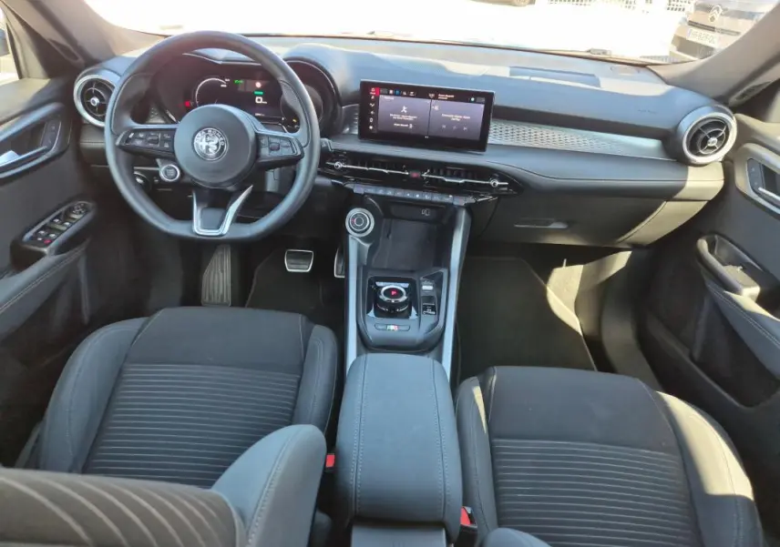 Vue intérieure frontale de l'Alfa Romeo Tonale 2025, tableau de bord moderne avec écran tactile et volant sport noir.