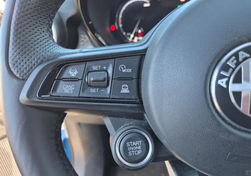 Gros plan sur le volant sport noir de l'Alfa Romeo Tonale bleu, avec commandes de régulateur et bouton start/stop visibles.