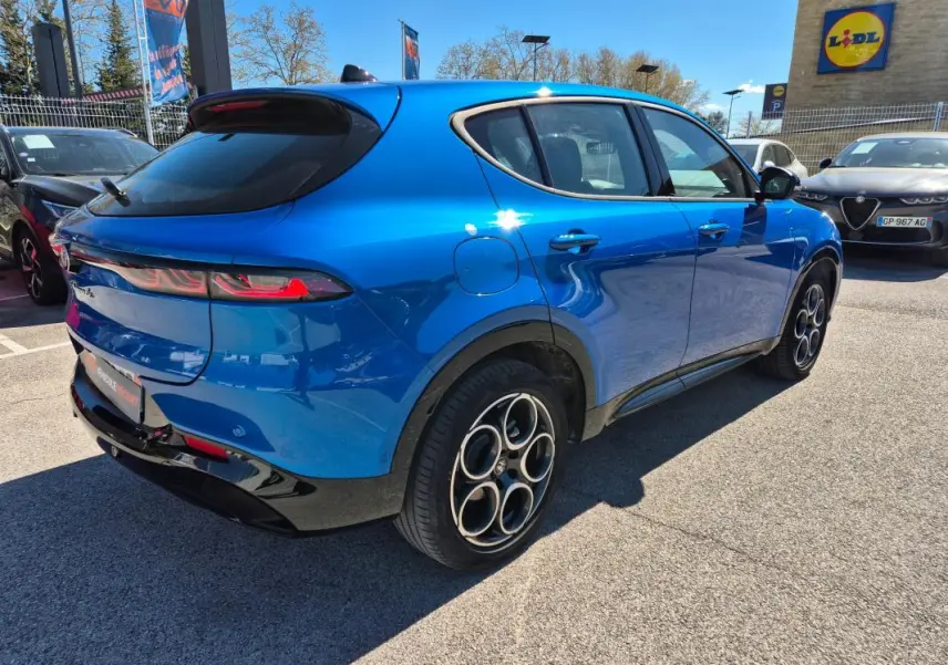 Vue 3/4 arrière droite d'une Alfa Romeo Tonale bleu avec jantes alliage 18 pouces et feux arrière allumés.