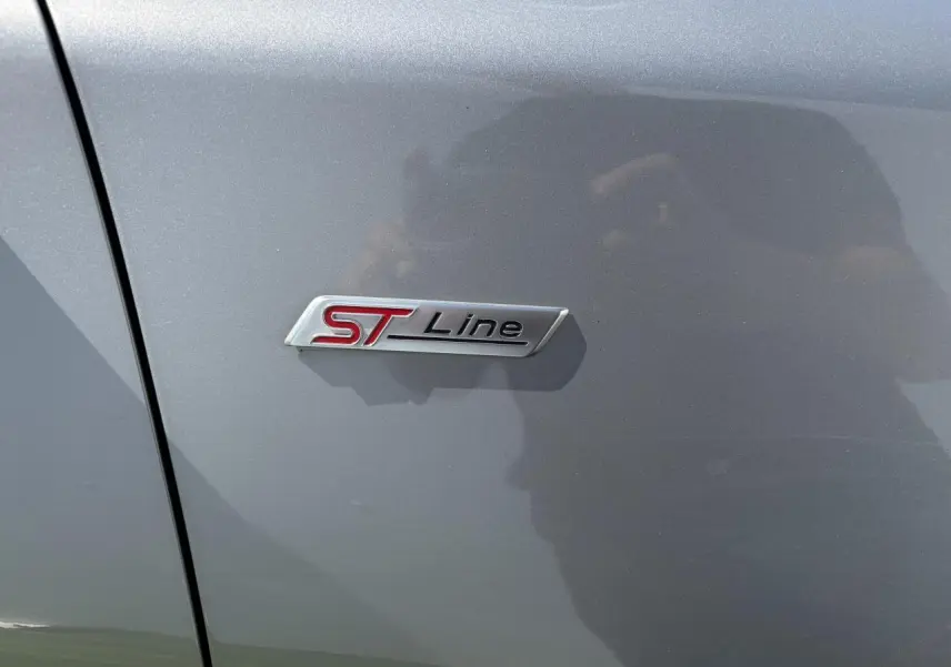 Gros plan sur le badge ST-Line rouge et argent sur la porte côté gauche d’un Ford Puma gris métal.