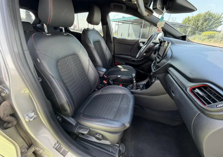 Vue intérieure côté conducteur du Ford Puma gris métal 2020, sièges noirs avec surpiqûres rouges et tableau de bord avec touches rouges.