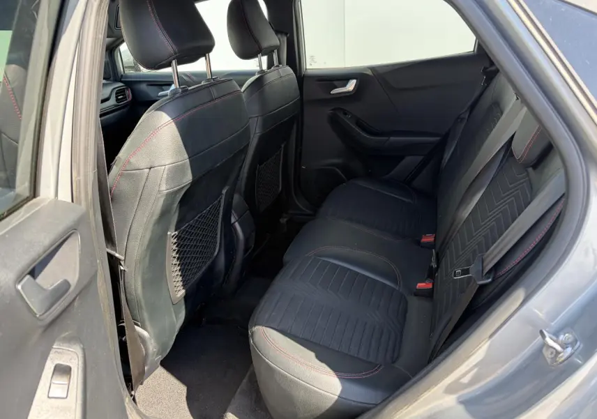 Vue côté gauche de l’intérieur arrière du Ford Puma gris métal, avec sièges noirs et surpiqûres rouges visibles.