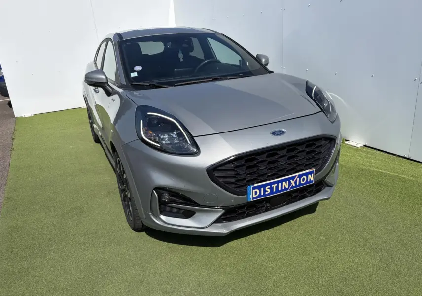 Vue 3/4 avant d'un Ford Puma gris métal avec calandre noire et jantes alliage noires sur sol vert.