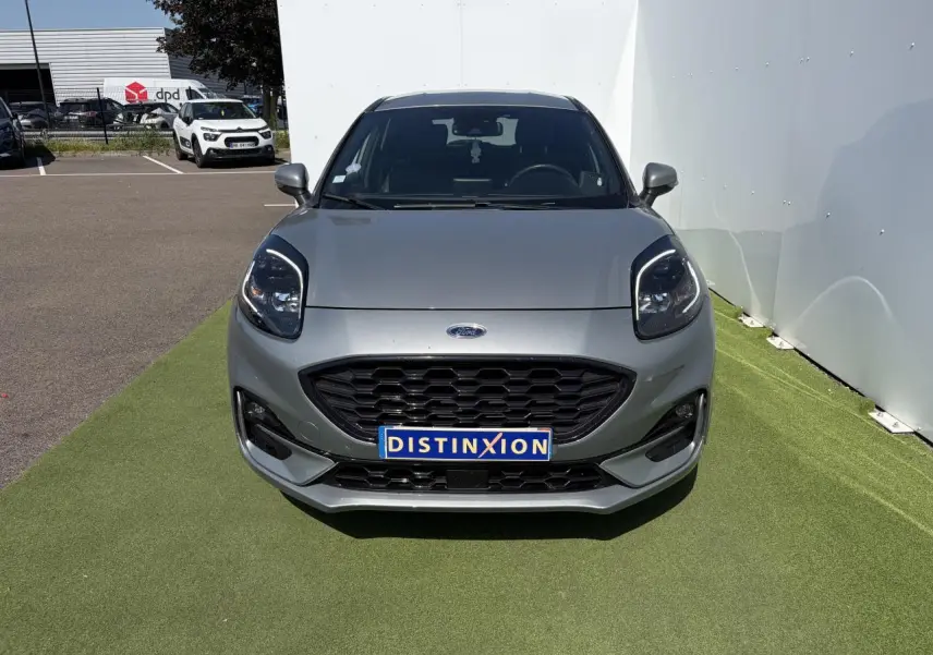 Vue avant d'un Ford Puma gris métal avec calandre noire et phares LED, sur fond d'herbe synthétique.