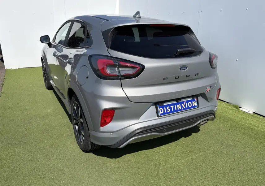 Vue 3/4 arrière droite d'un Ford Puma gris métal avec badges ST-Line et jantes alliage noires sur fond vert.