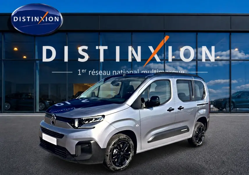 Vue 3/4 avant droit d'un Citroën Berlingo gris acier avec jantes noires devant une vitrine Distinxion.