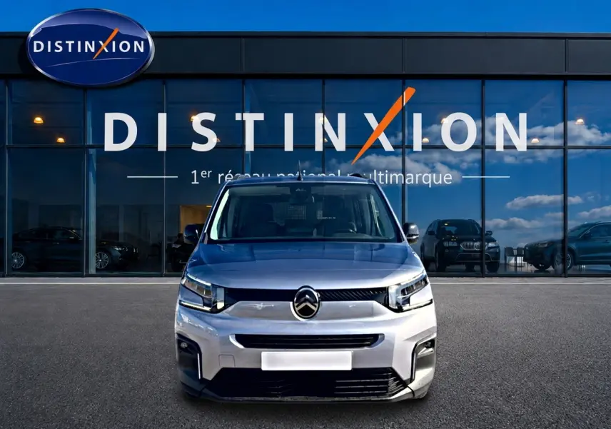 Vue frontale d'un Citroën Berlingo 2026 gris acier, avec calandre distinctive et logo centré devant un showroom Distinxion.