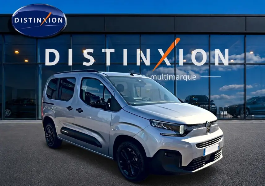 Vue 3/4 avant droit du Citroën Berlingo gris steel avec barres de toit et jantes noires devant un showroom Distinxion.