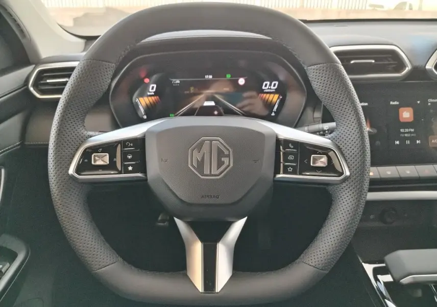 Vue frontale du volant perforé noir du MG MOTOR ZS 1.5 l Hybrid + 197 LUXURY avec tableau de bord numérique et écran tactile.