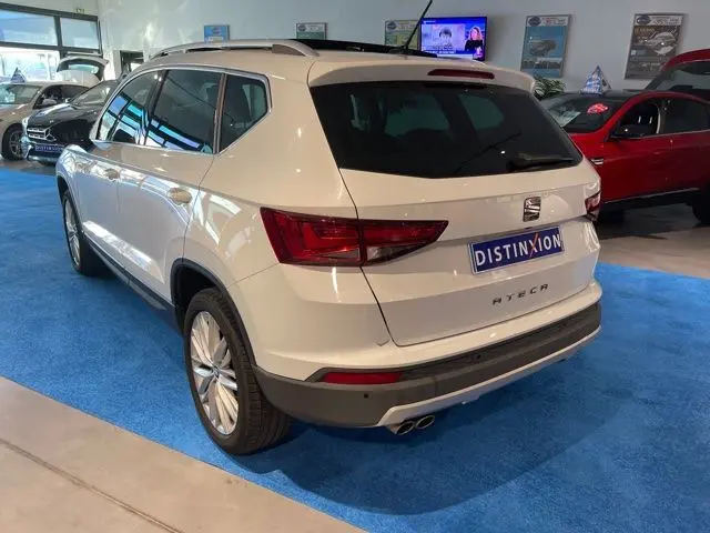 Vue 3/4 arrière droite d'un SEAT Ateca blanc Nevada en showroom, avec jantes alliage et vitres teintées.