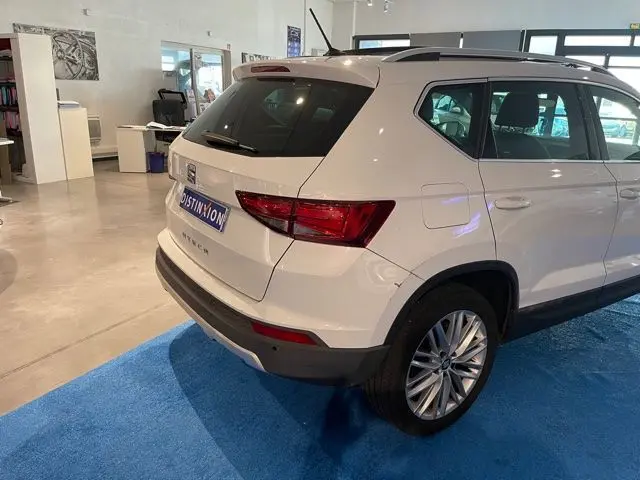 Vue 3/4 arrière droite d'un SEAT Ateca blanc Nevada exposé en intérieur sur tapis bleu.