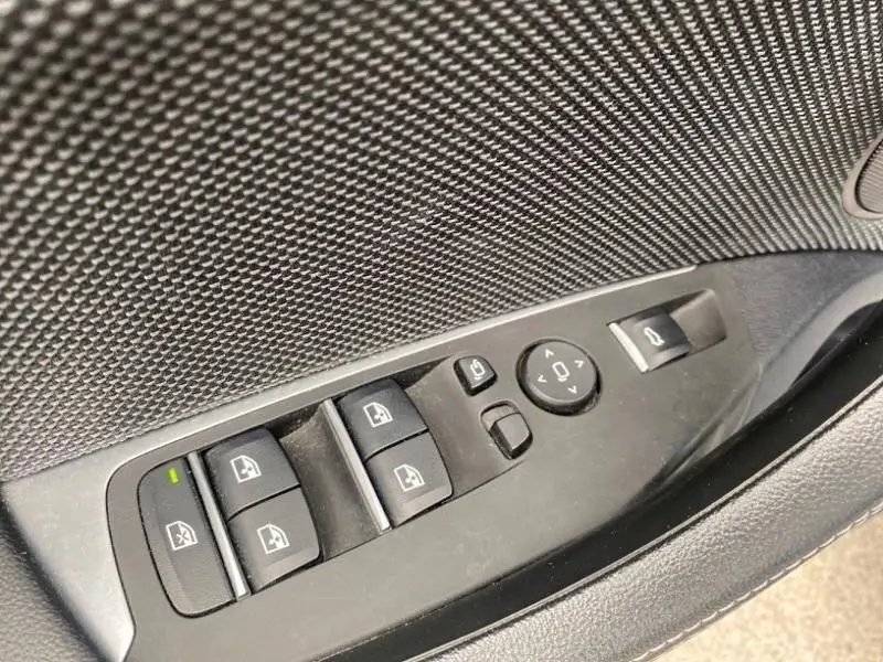 Gros plan sur les commandes de lève-vitres et réglages des rétroviseurs côté conducteur d’un BMW X3 bleu métal 2018.